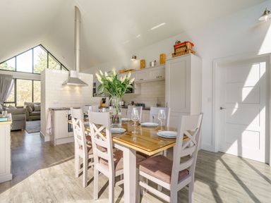 A kitchen and dining area with a wooden table set for six and a living room with large windows at Wood Sage in Bamburgh