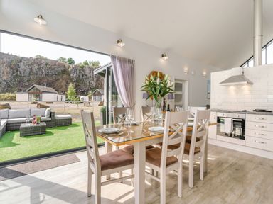 A dining area with a table set for six next to a kitchen with white cabinets and an outdoor seating area at Wood Sage in Bamburgh