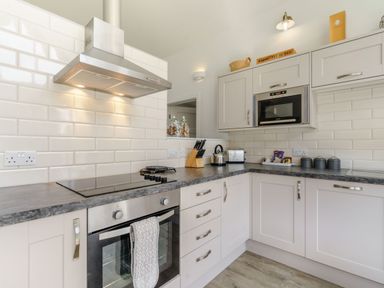 A kitchen with white cabinets black countertop built-in oven microwave toaster kettle and knife block at Wood Sage in Bamburgh