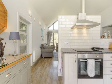 A kitchen with an oven and stovetop next to a living room with gray sofas and large windows at Wood Sage Bamburgh