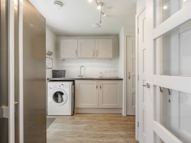 A utility room with a washing machine sink cupboards and a refrigerator at Wood Sage in Bamburgh