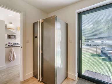 A kitchen corner with a stainless steel refrigerator and a glass door with blinds at Wood Sage in Bamburgh