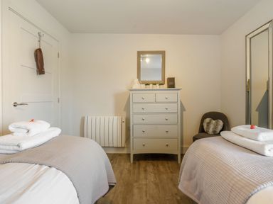 A bedroom with two single beds a chest of drawers a wall mirror and a chair at Wood Sage in Bamburgh