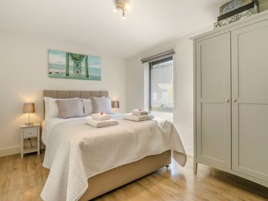 A bedroom with a bed two bedside tables with lamps a wardrobe and a window with blinds at Wood Sage in Bamburgh