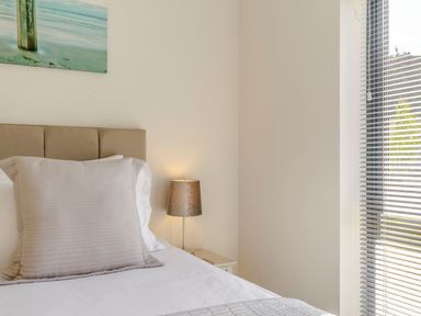 A bed with beige pillow and headboard near a lamp and window with blinds in a bedroom at Wood Sage in Bamburgh