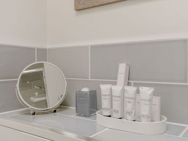 A bathroom counter with a round mirror cotton balls and toiletry bottles at Wood Sage in Bamburgh