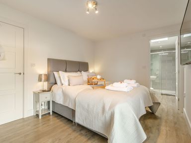 A bedroom with a bed with white linens and towels a bedside table and a lamp next to an open door to a bathroom at Wood Sage in Bamburgh