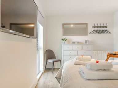 A bedroom with a tv on the wall a chair a dresser with a mirror above and towels on the bed at Wood Sage in Bamburgh