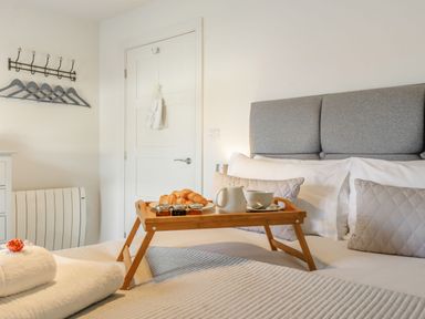 A bedroom with a grey headboard bed tray with croissants teapot and cups and folded towels on the bed at Wood Sage in Bamburgh