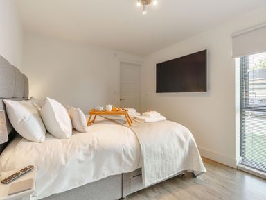 A bedroom with a bed with white linens a wooden tray with breakfast items a wall-mounted television and a window with blinds at Wood Sage in Bamburgh