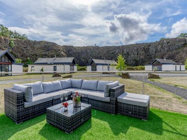 An outdoor seating area with a sectional sofa and table with glasses and a bottle on artificial grass at Wood Sage in Bamburgh