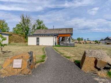 A pathway leading to a single-story lodge with a porch and outdoor seating at Wood Sage in Bamburgh