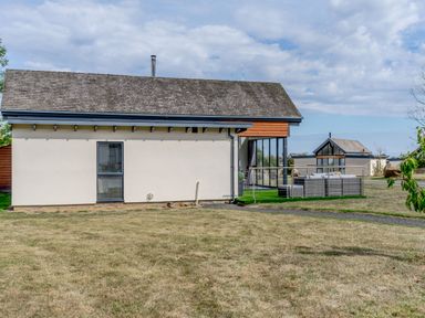 A modern single-story house with a small patio and outdoor seating in a grassy yard at Wood Sage in Bamburgh