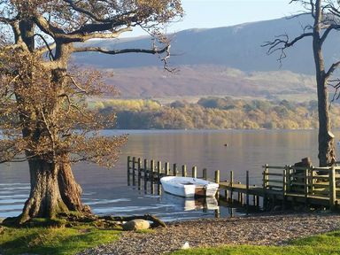 A lake with a wooden dock and a small white boat near trees at Low House in Ullswater