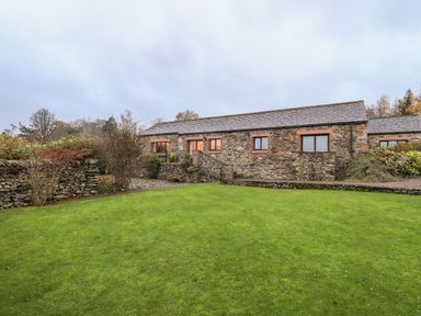 A stone house with multiple windows and a green lawn in front at Low House in Ullswater