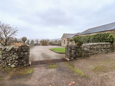 An entrance gate with stone pillars and a cattle grid leading to a stone building and driveway at Low House in Ullswater