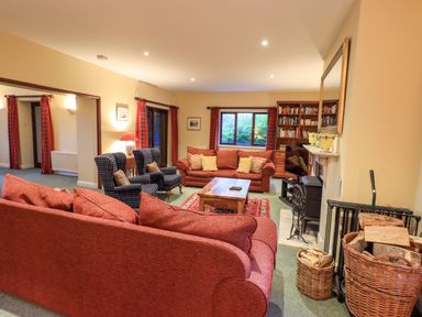 A living room with red sofas two armchairs a wooden coffee table a fireplace and bookshelves at Low House in Ullswater
