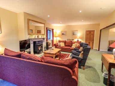 A living room with red sofas, armchairs, a wooden coffee table, a fireplace, and a large mirror at Low House in Ullswater