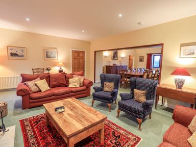 A living room with red sofas two armchairs a wooden coffee table and a dining area in the background at Low House in Ullswater