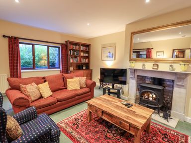 A living room with a red sofa a wooden coffee table a fireplace and a window with red curtains at Low House in Ullswater