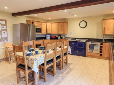 A kitchen with wooden cabinets a large stainless steel refrigerator a wooden dining table with chairs and a tablecloth with dishes on it at Low House Ullswater