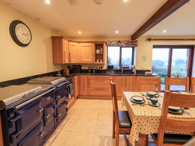 A kitchen with wooden cabinets a blue stove a dining table set with cups and plates and a clock on the wall at Low House in Ullswater