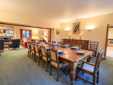 A dining room with a long wooden table set with plates and glasses connected to a sitting room with armchairs and sofas at Low House in Ullswater