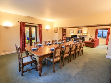 A dining room with a long wooden table set with plates and glasses next to a sitting room with sofas and a fireplace at Low House in Ullswater