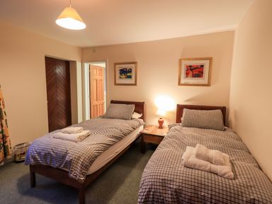 A bedroom with two single beds with checkered bedding and towels on top a bedside table with a lamp and two framed pictures on the wall at Low House in Ullswater