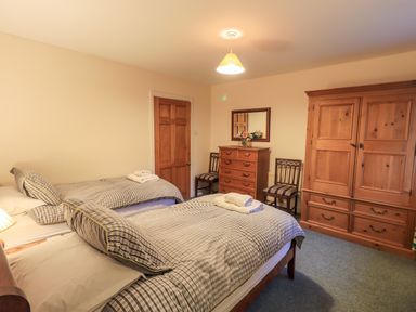 A bedroom with two beds a wooden wardrobe a chest of drawers and two chairs at Low House in Ullswater