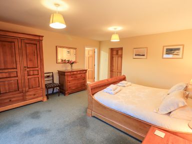A bedroom with a bed towels on the bed a wooden wardrobe a dresser a chair and framed pictures on the wall at Low House in Ullswater