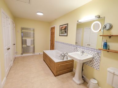 A bathroom with a bathtub wooden panel sink wall mirror towel rack and toilet at Low House in Ullswater