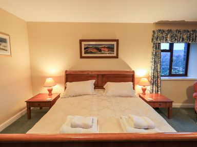 A bedroom with a wooden bed two bedside tables with lamps a window with curtains and paintings on the walls at Low House in Ullswater