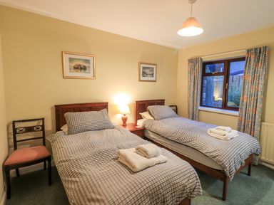 A bedroom with two single beds with checkered bedding and towels on them a chair bedside table and window with floral curtains at Low House in Ullswater