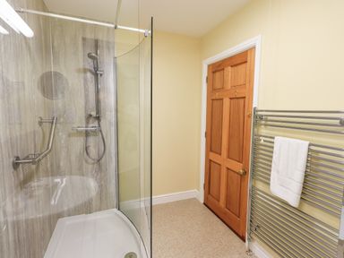 A bathroom with a curved glass shower enclosure wooden door and a chrome towel radiator with a white towel at Low House in Ullswater