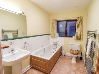 A bathroom with a pedestal sink, bathtub with wooden panel, toilet with wooden seat, window with curtains and heated towel rail at Low House Ullswater