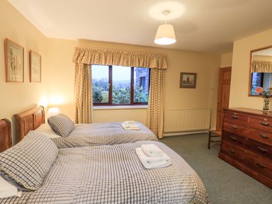 A bedroom with two single beds a wooden dresser a window with curtains and framed pictures on the wall at Low House in Ullswater