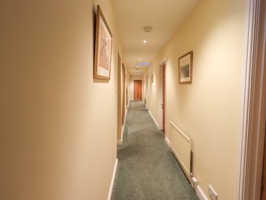 A hallway with green carpet multiple wooden doors framed pictures and a radiator at Low House Ullswater
