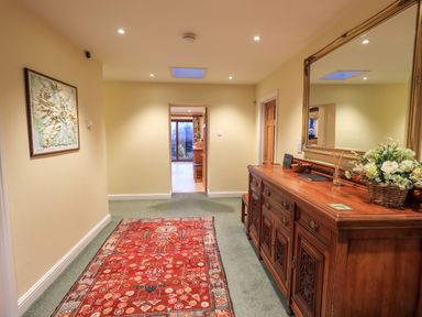 A hallway with a red patterned rug a wooden sideboard with a large mirror and a basket of flowers on it at Low House Ullswater