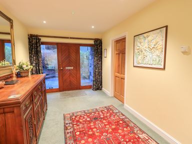 An entryway with a wooden dresser with flowers and a mirror and a red patterned rug in front of a wooden door and a framed map on the wall at Low House in Ullswater