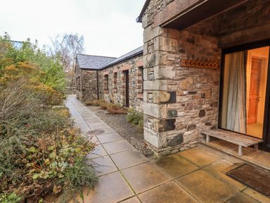 A stone exterior wall of a building with a wooden bench near a door and a stone tiled walkway surrounded by plants at Low House in Ullswater