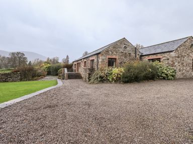 A stone building with slate roof surrounded by gravel driveway and lawn at Low House in Ullswater