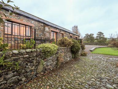 A stone building with metal railings and outdoor seating overlooking a cobblestone path and grassy area at Low House in Ullswater