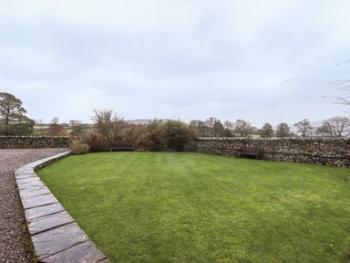 A grassy garden area with two wooden benches and stone walls at Low House in Ullswater
