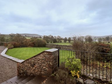 An outdoor garden with green grass stone wall and bench overlooking fields and trees at Low House in Ullswater