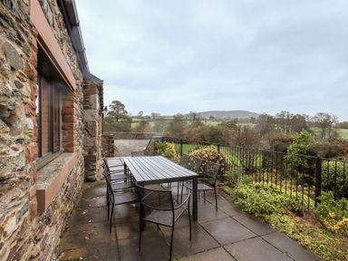 An outdoor patio with black metal table and chairs next to a stone house with garden and countryside view at Low House in Ullswater