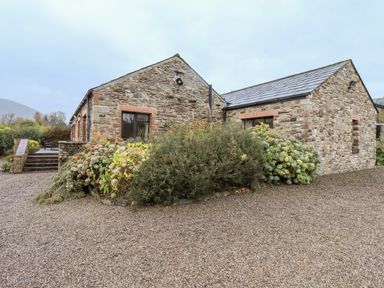 A stone house with gravel driveway and shrubs in front at Low House in Ullswater
