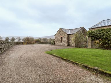 A gravel driveway with a stone building and a small lawn area surrounded by stone walls at Low House in Ullswater