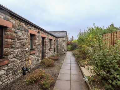 A stone wall building with windows and a door next to a paved pathway with bushes at Low House in Ullswater