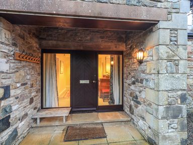 A stone entrance with a dark wooden door flanked by glass panels a wooden bench and a wall-mounted light at Low House in Ullswater